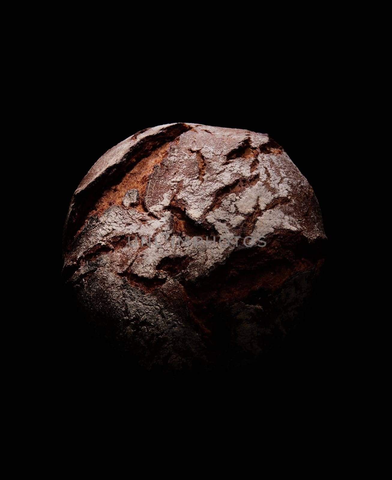 From above of baked round shaped loaf of bread with crispy crust placed on black background in studio with dim light