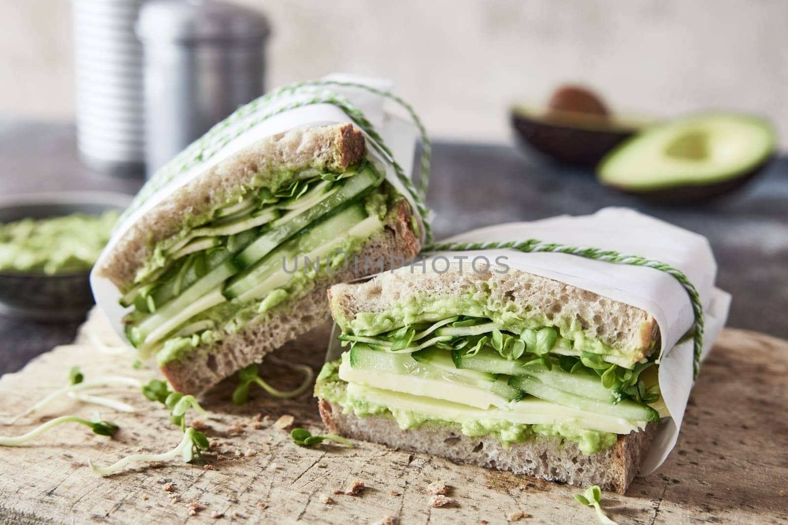 Appetizing homemade vegetarian sandwiches with guacamole and cucumbers served on wooden cutting board in kitchen