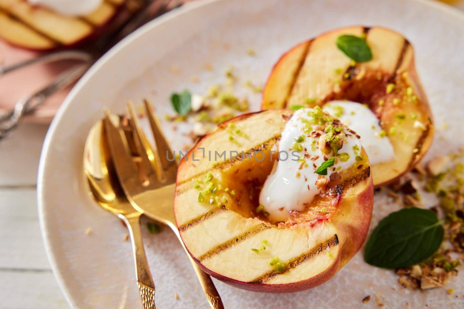 High angle closeup of sweet dessert with grilled nectarines and yogurt garnished with mint and sprinkled with pistachios placed on wooden table