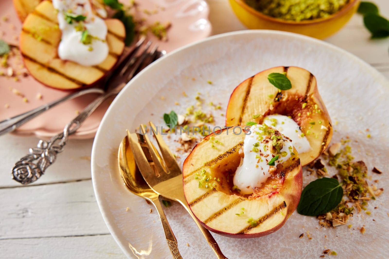 From above of ripe grilled peaches with yogurt and green pistachio sprinkle served with cutlery on table