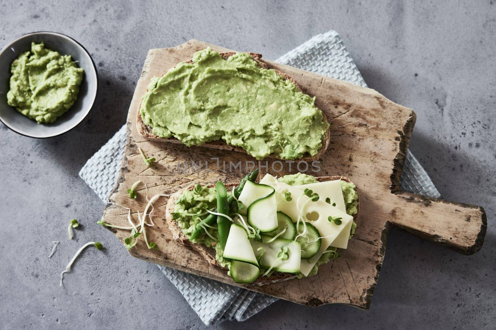 Top view of appetizing toasts with guacamole and cucumbers and cheese served on rustic wooden board on concrete table