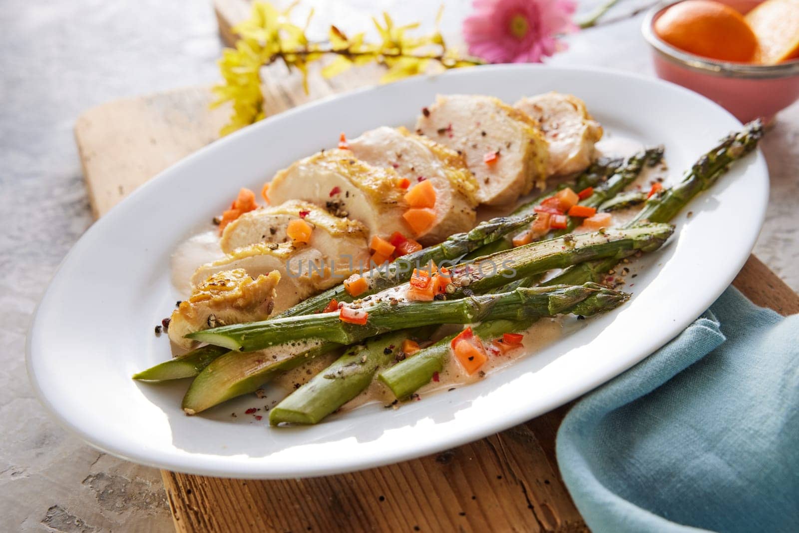 High angle of plate with appetizing cut chicken breast with asparagus and carrots served on wooden board for lunch