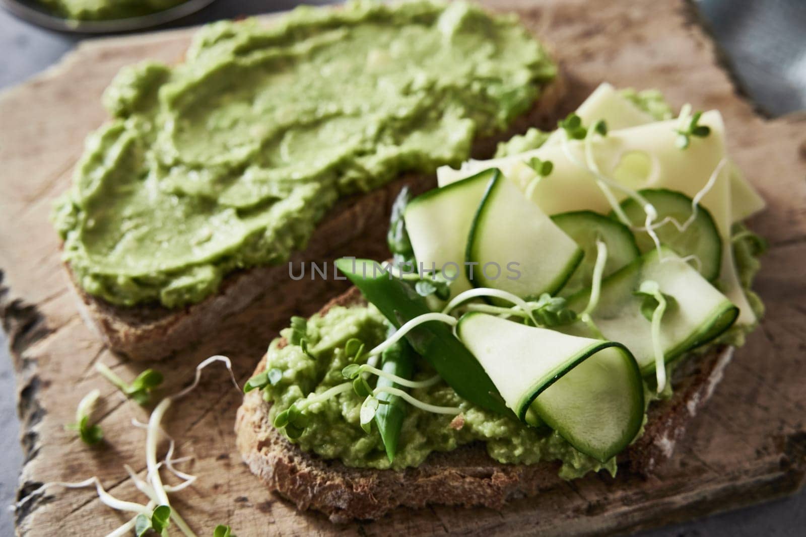 High angle closeup of yummy bruschettas with guacamole and cucumbers and cheese slices placed on cutting board