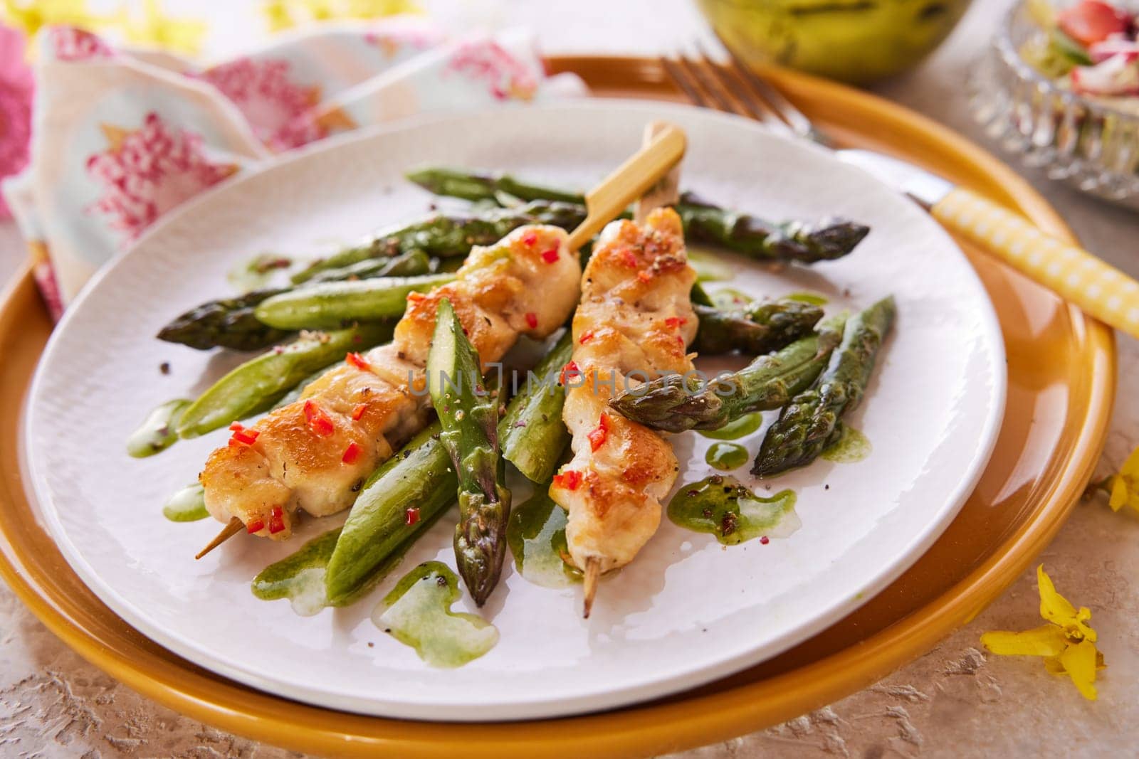 High angle of yummy chicken on wooden skewers served with fresh asparagus on plate for lunch on table