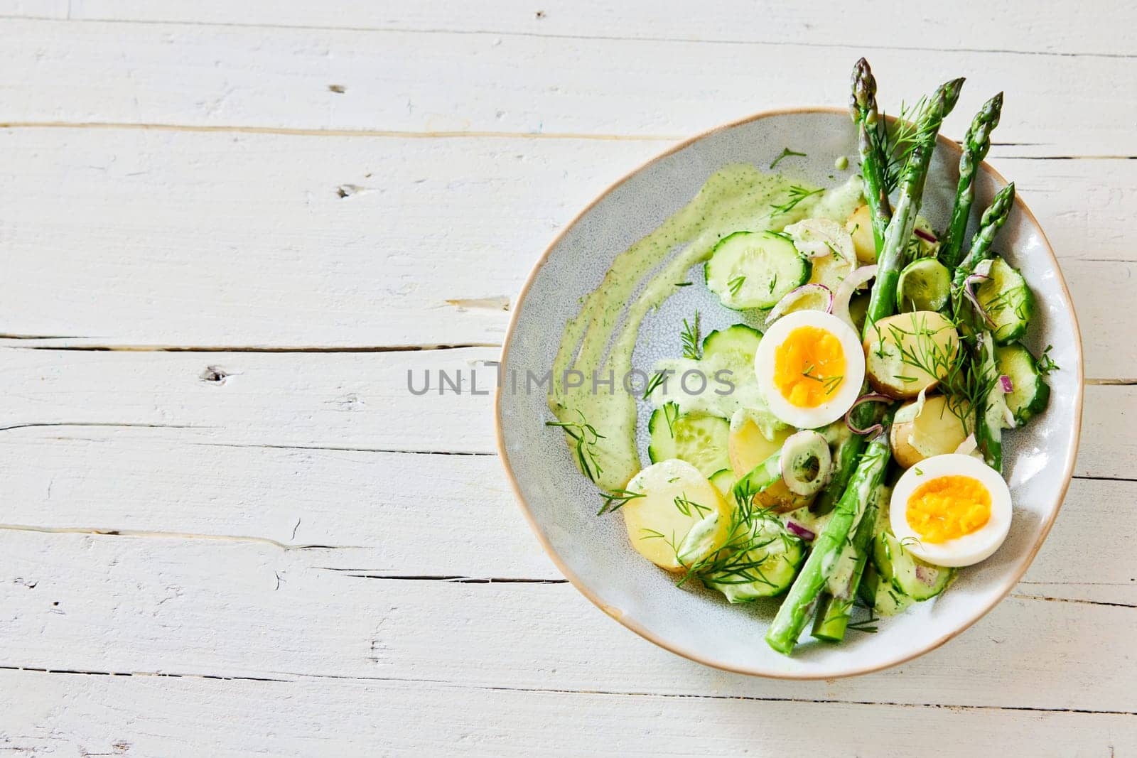 Top view of appetizing fresh asparagus salad with boiled eggs and potatoes served on plate on wooden table
