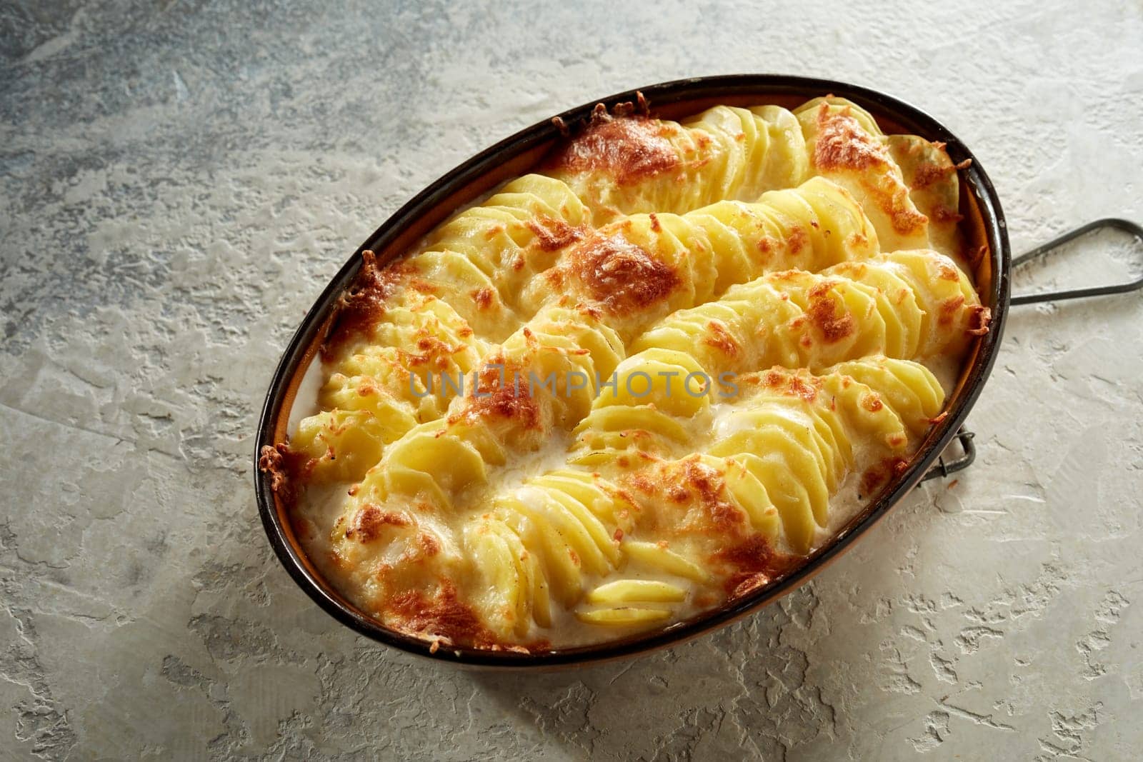 From above of casserole with tasty potato gratin with cheese served on gray concrete background