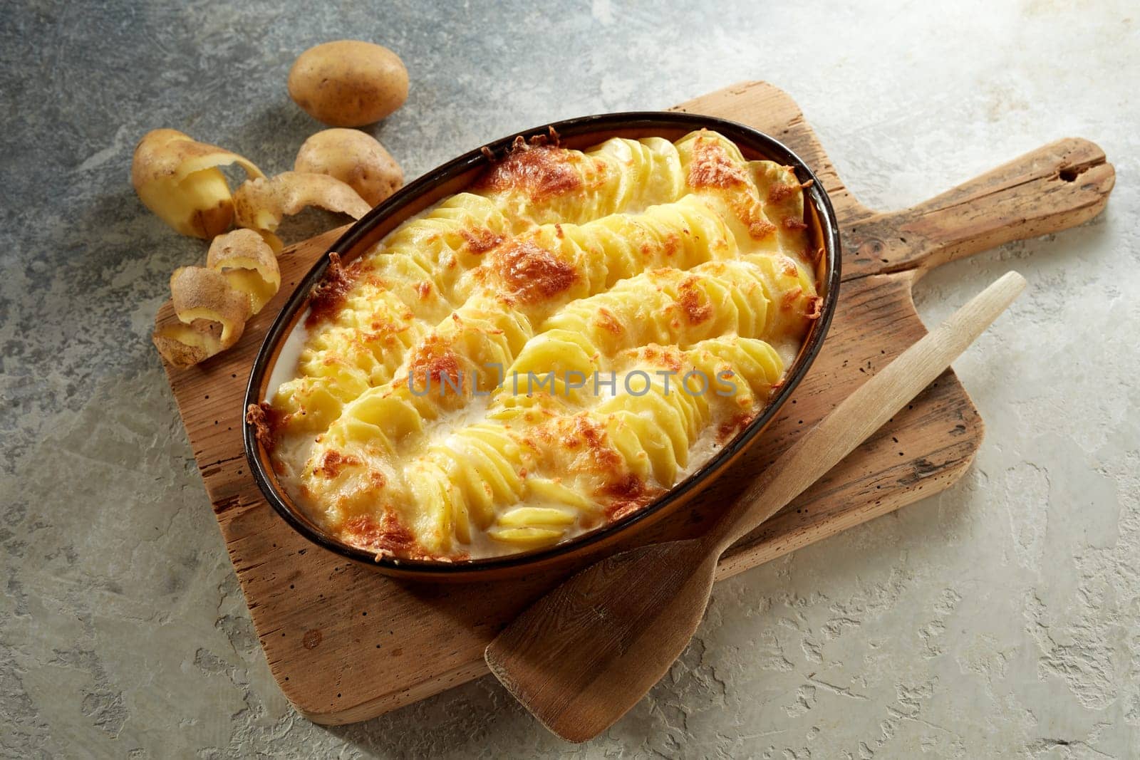 From above of appetizing potatoes au gratin dish prepared on casserole pan and served on wooden cutting board on gray table in kitchen
