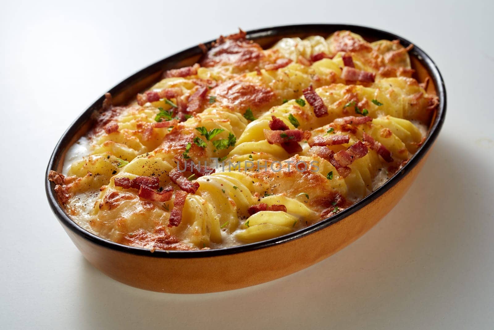 High angle of palatable gratin au potato with crispy baked cheese and bacon pieces served on white table in daylight