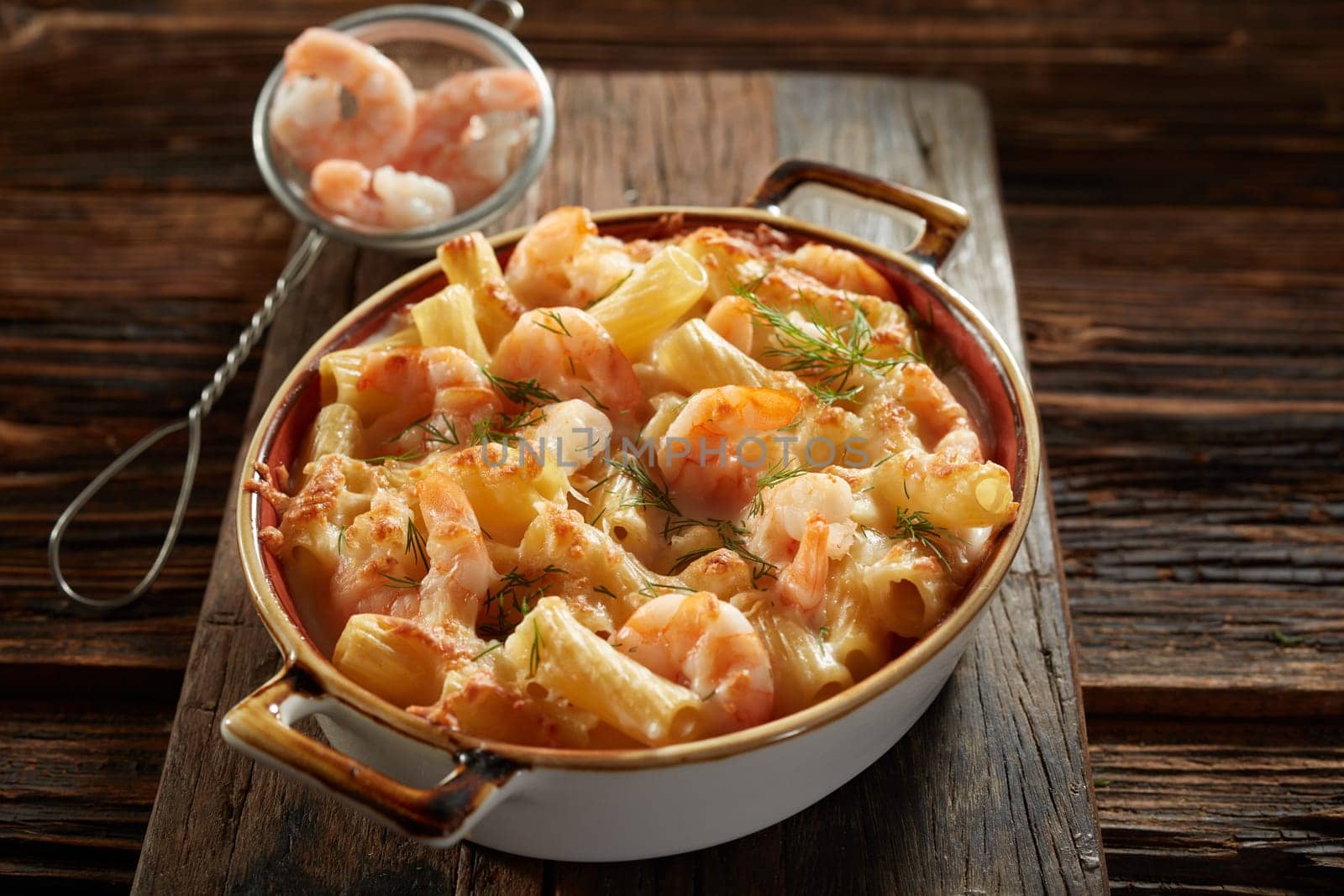 From above of delicious rigatoni pasta with shrimps and sauce prepared in saucepan and decorated with herbs in kitchen