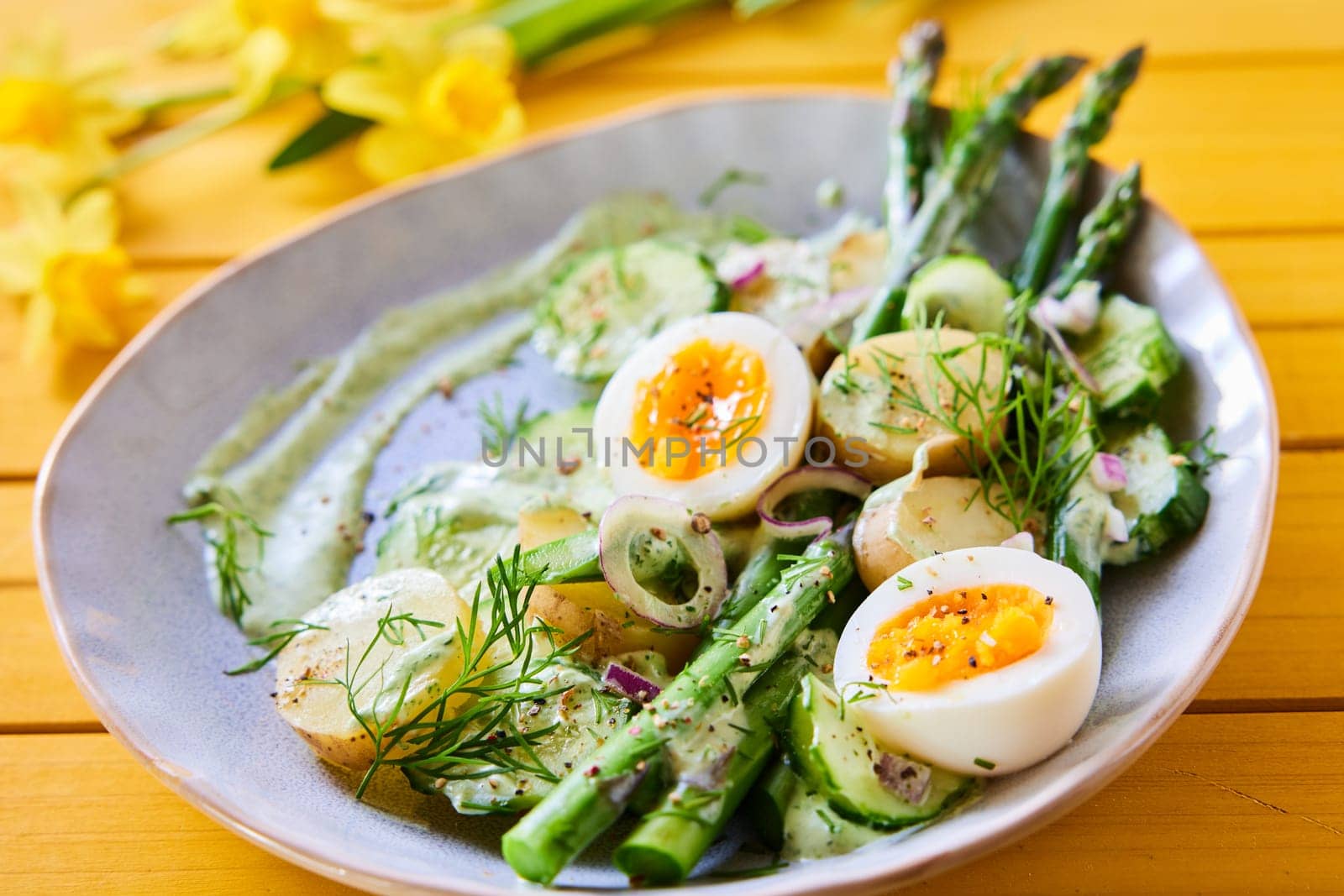 From above of yummy spring salad with ripe asparagus and boiled eggs with potatoes placed on table with flowers for lunch