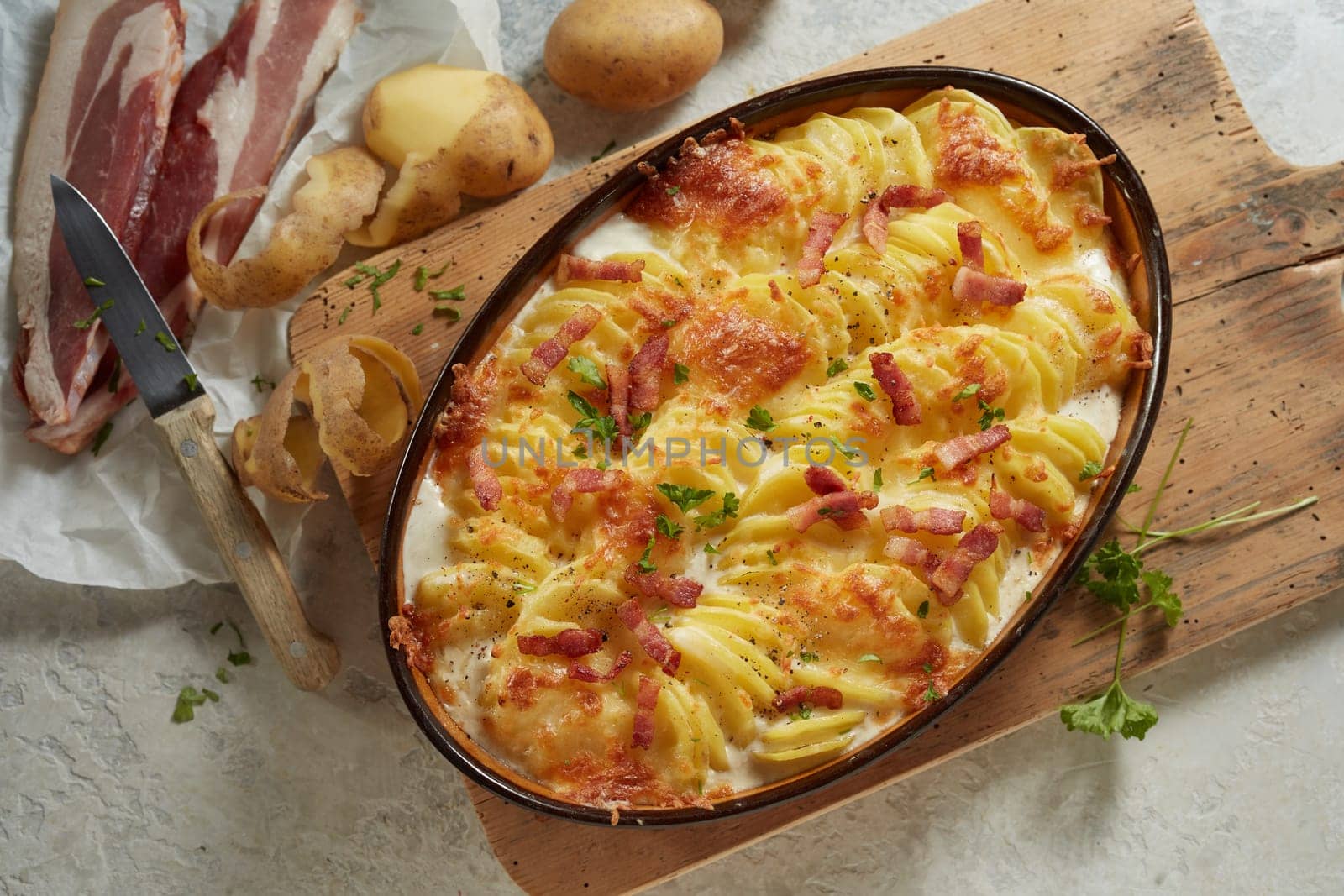 Top view of oval pan with appetizing potato gratin with cheese and bacon served on wooden cutting board on table in kitchen