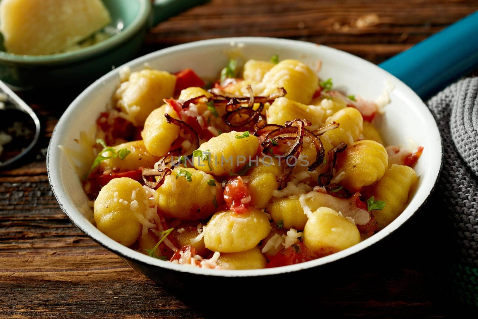 High angle of appetizing traditional Italian potato gnocchi served with stewed tomato fried onion and cheese in bowl on wooden table
