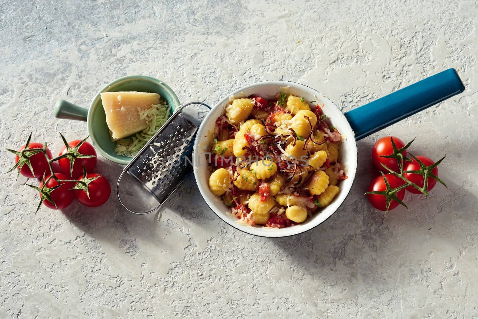 Top view of tasty potato gnocchi in pan served with ripe tomatoes and cheese on white concrete background