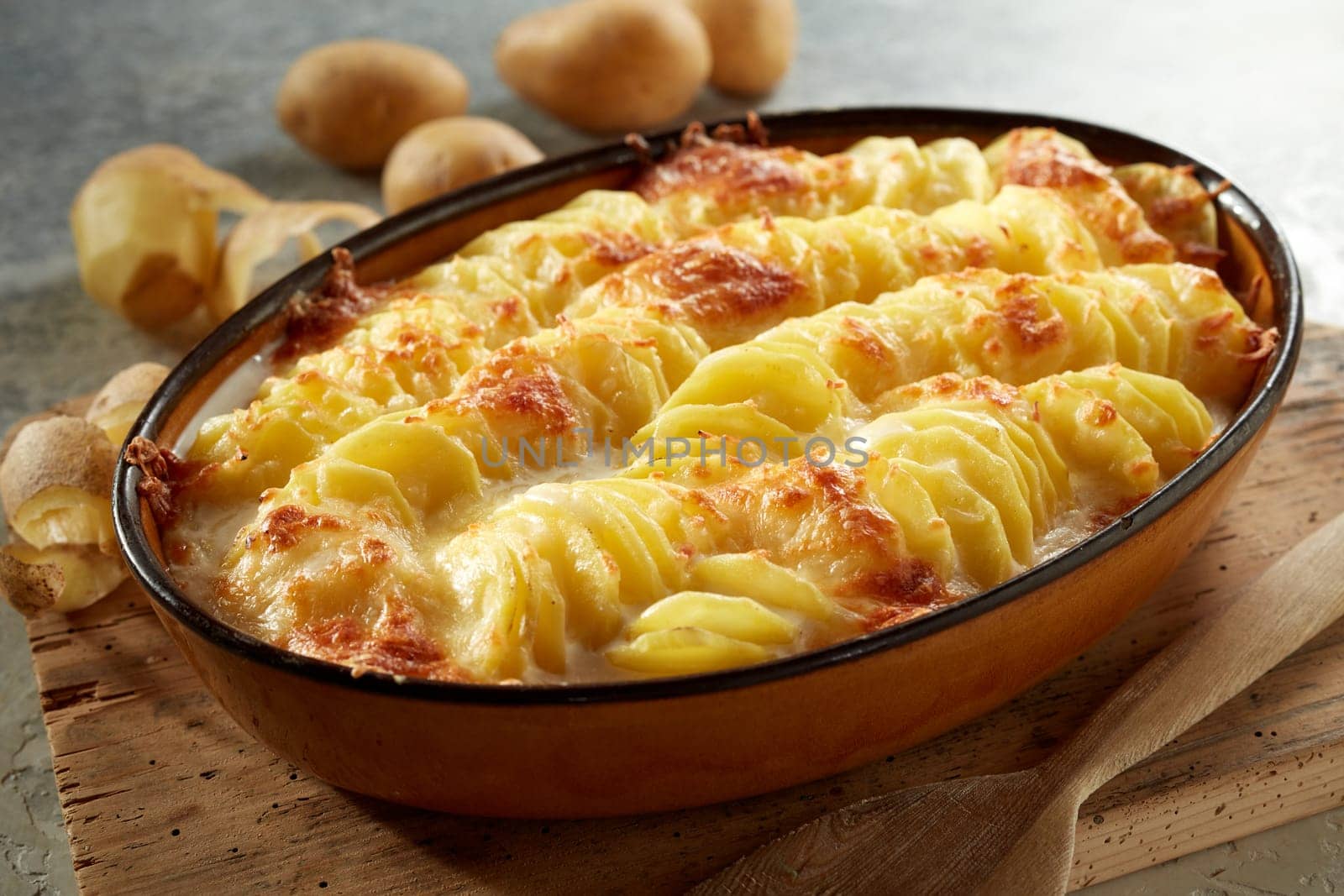 High angle of delicious gratin with potato and cheese with crispy crust prepared in casserole pan and served on wooden cutting board in kitchen