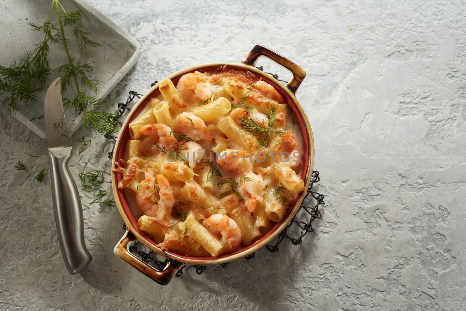 From above of delicious homemade creamy pasta with seafood and cheese served on gray table near sharp knife and dill branch in kitchen