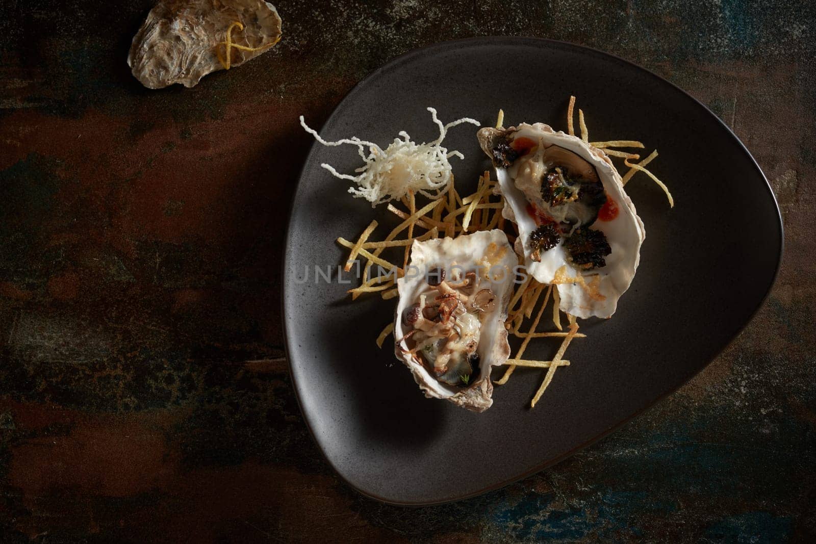 Top view of appetizing expensive open oysters served on black plate on shabby table