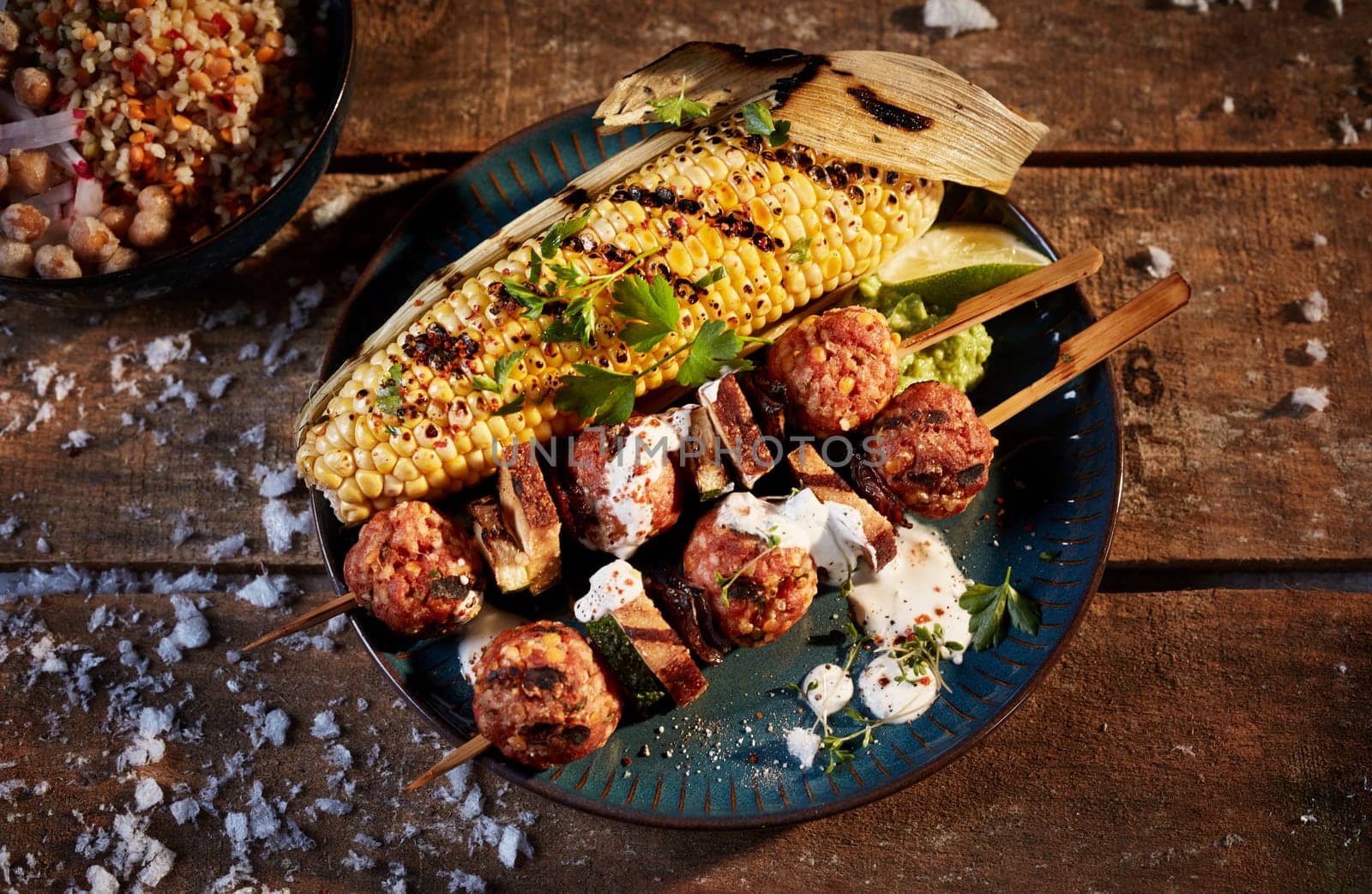 Top view of appetizing BBQ corn and meat balls on wooden sticks served with sauce and parsley leaves on wooden table with snow