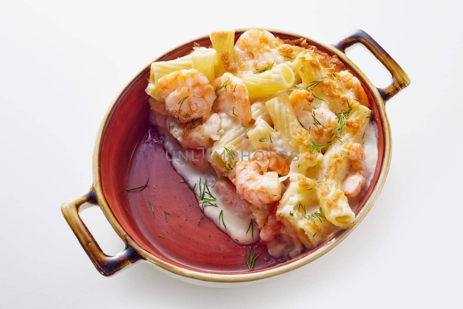 From above of appetizing rigatoni pasta baked in casserole with shrimps and creamy sauce and decorated with herbs on white table