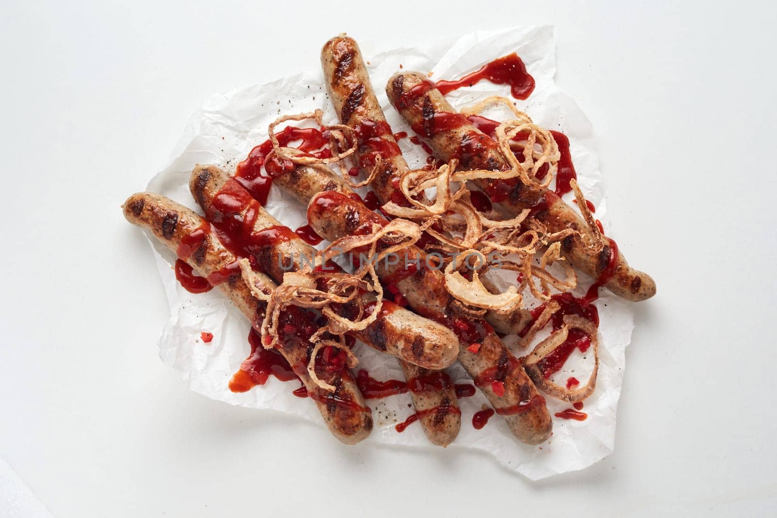 Top view of appetizing homemade grilled sausages served with onions and tomato sauce against white background