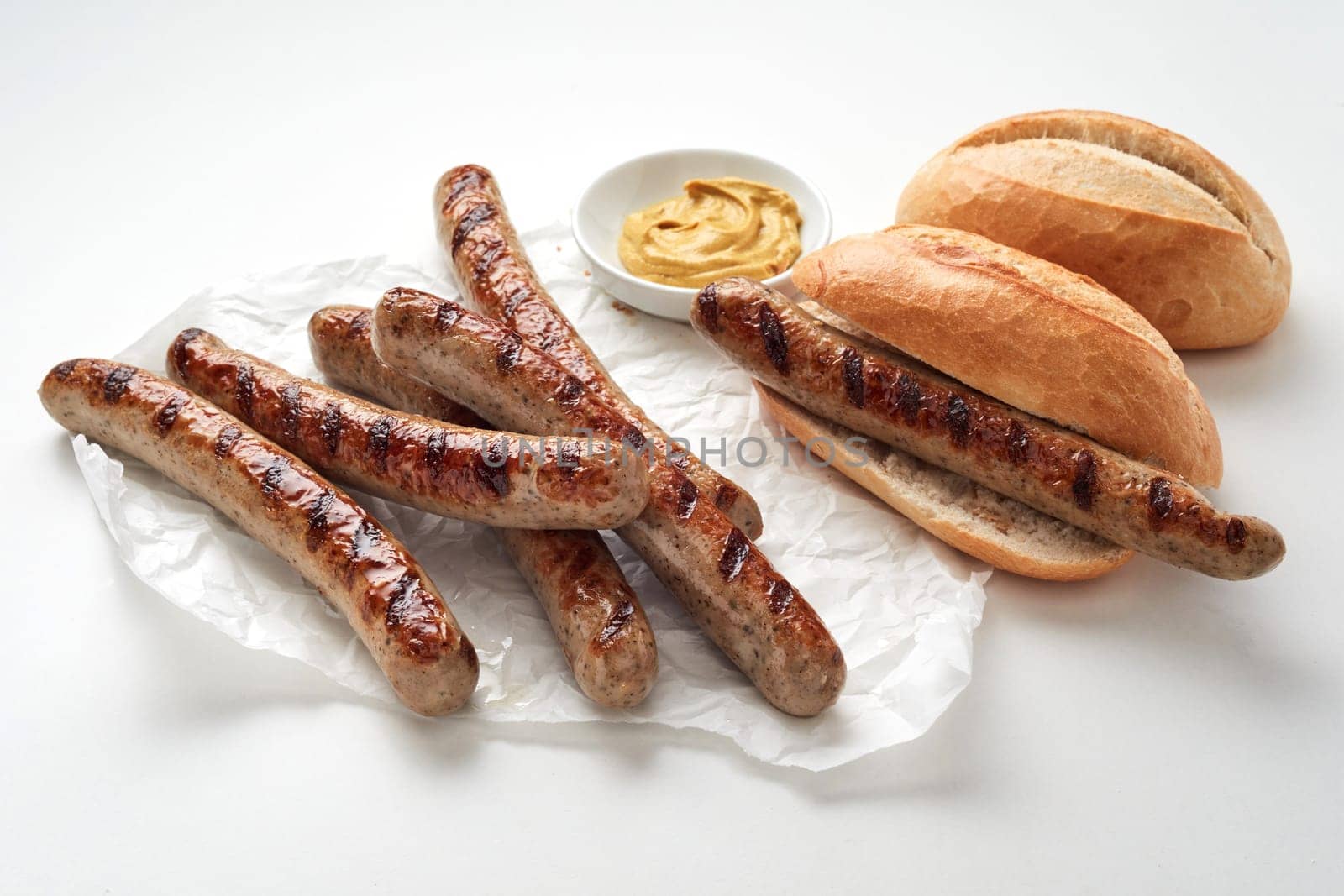 Tasty grilled sausages and fresh bread placed near bowl with sauce against light background