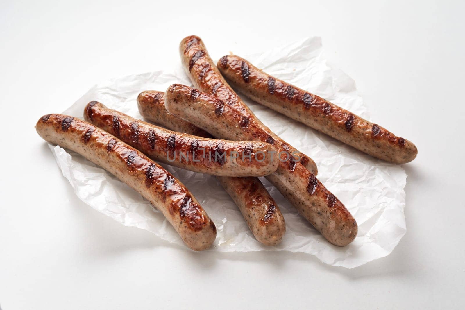 From above of delicious sausages placed on crumpled paper napkin against white background