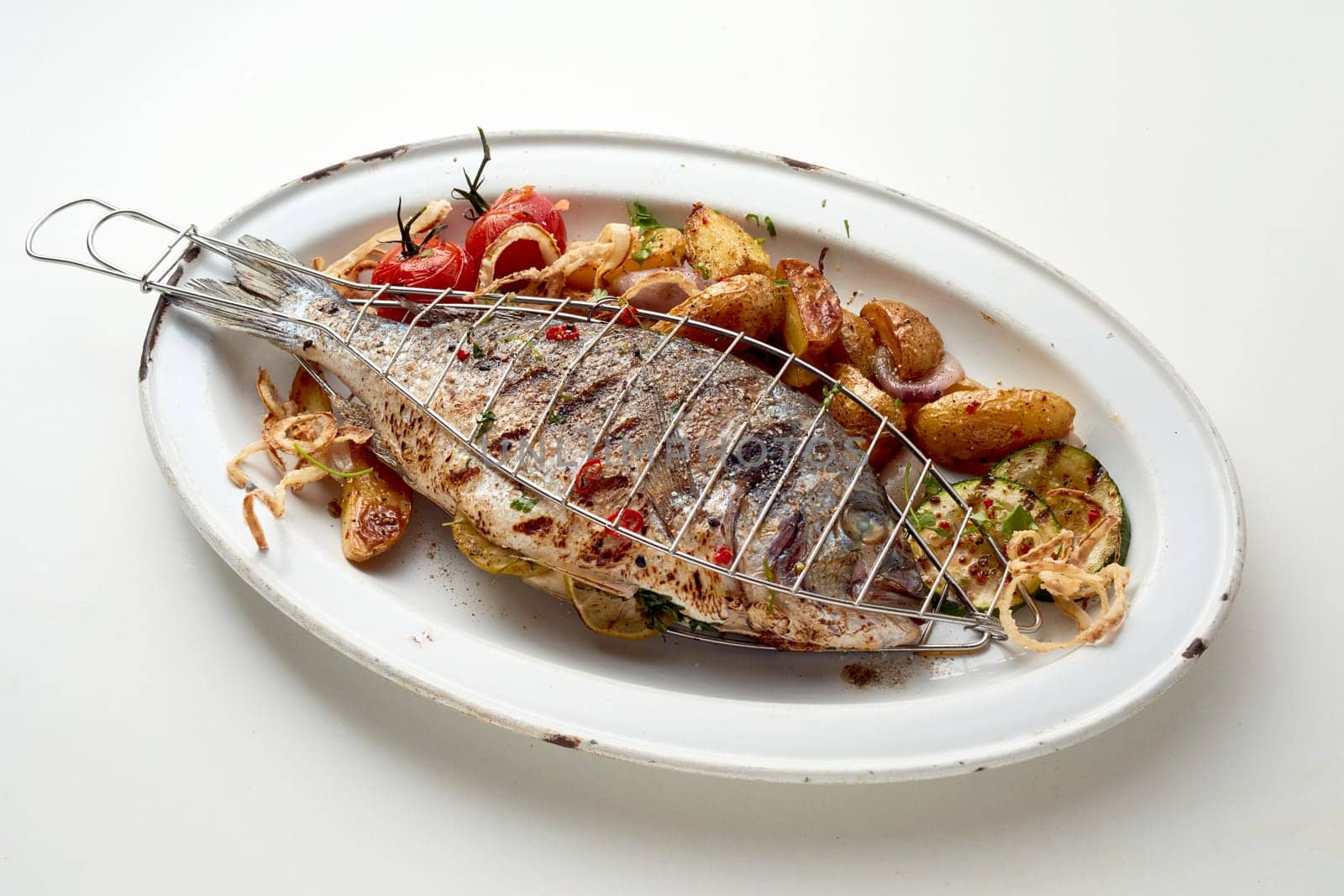 From above of tasty grilled fish served with vegetables and potatoes on while plate placed in table