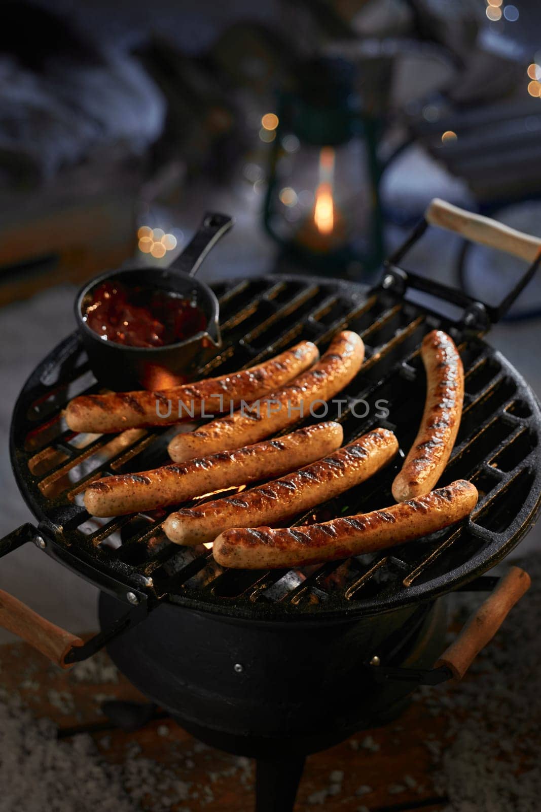 High angle of appetizing grilled sausages with sauce on metal barbecue grid on backyard at night