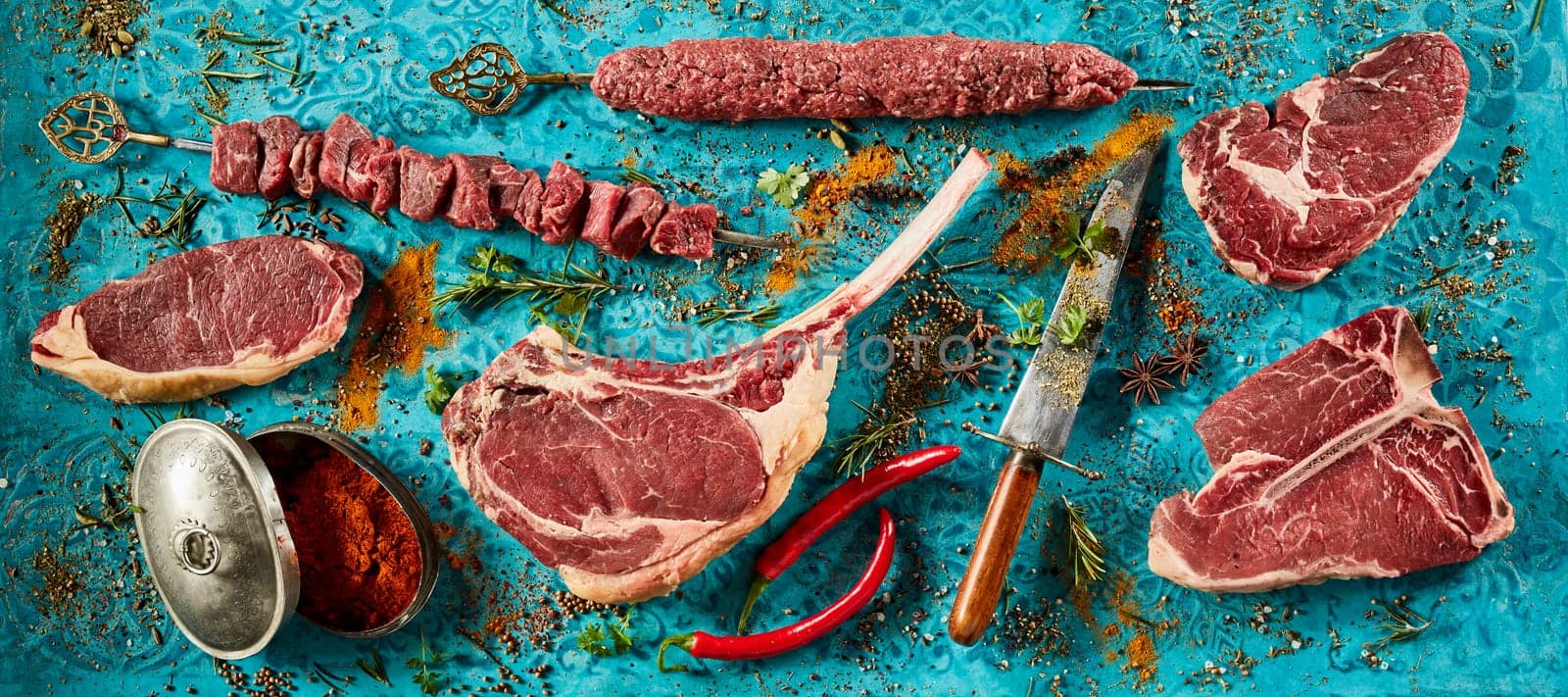 Top view arrangement of fresh raw meat steaks and chili peppers placed on blue table