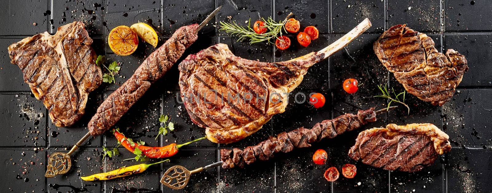 From above of tasty grilled meat steaks placed on black wooden table with spicy red chili peppers and tomatoes