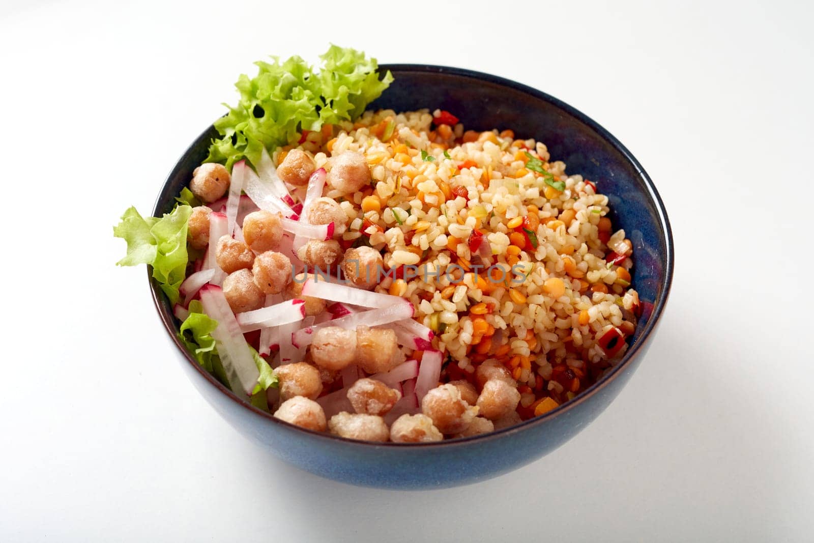 High angle of tasty bulgur salad with pieces of radish meat and lettuce leaf in bowl on white table