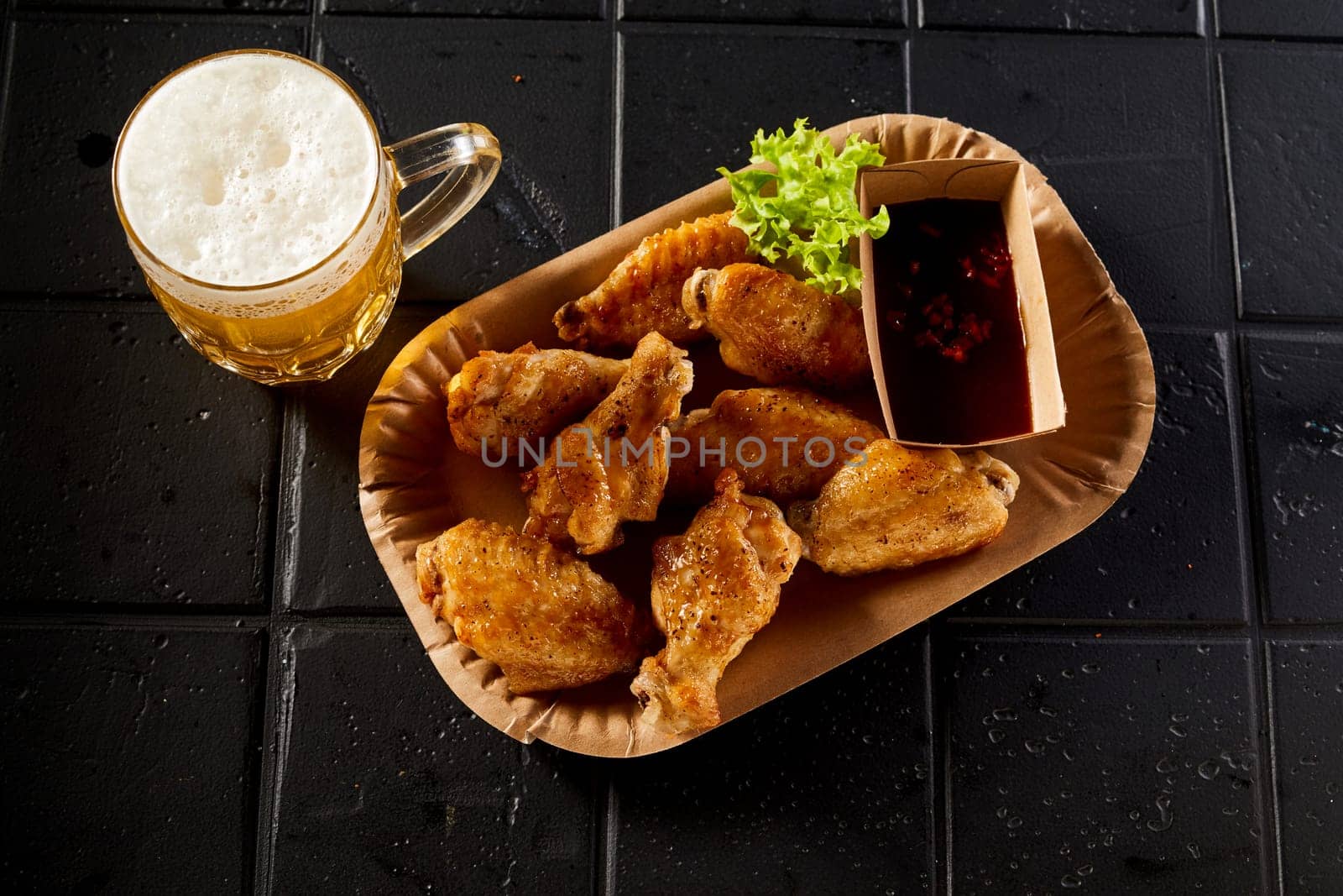 From above of plate with fried chicken wings with sauce and jar of beer placed on black table in restaurant