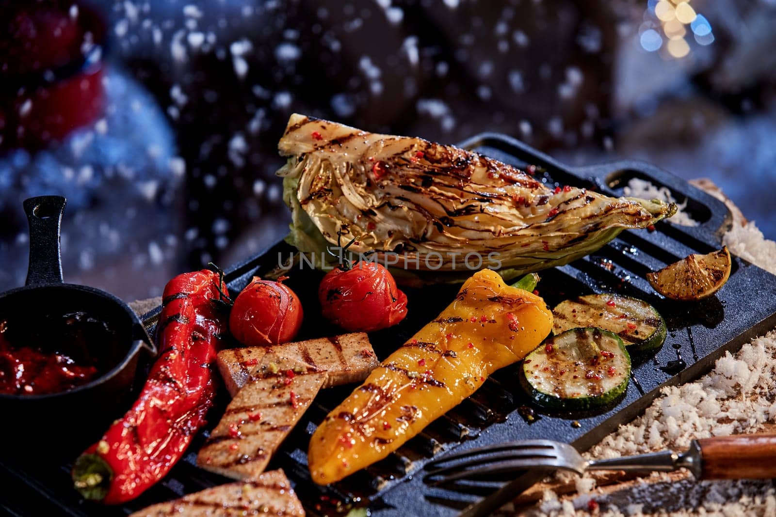 High angle of tasty BBQ cabbage red and yellow pepper with slices of zucchini and meat with ketchup in winter yard at night