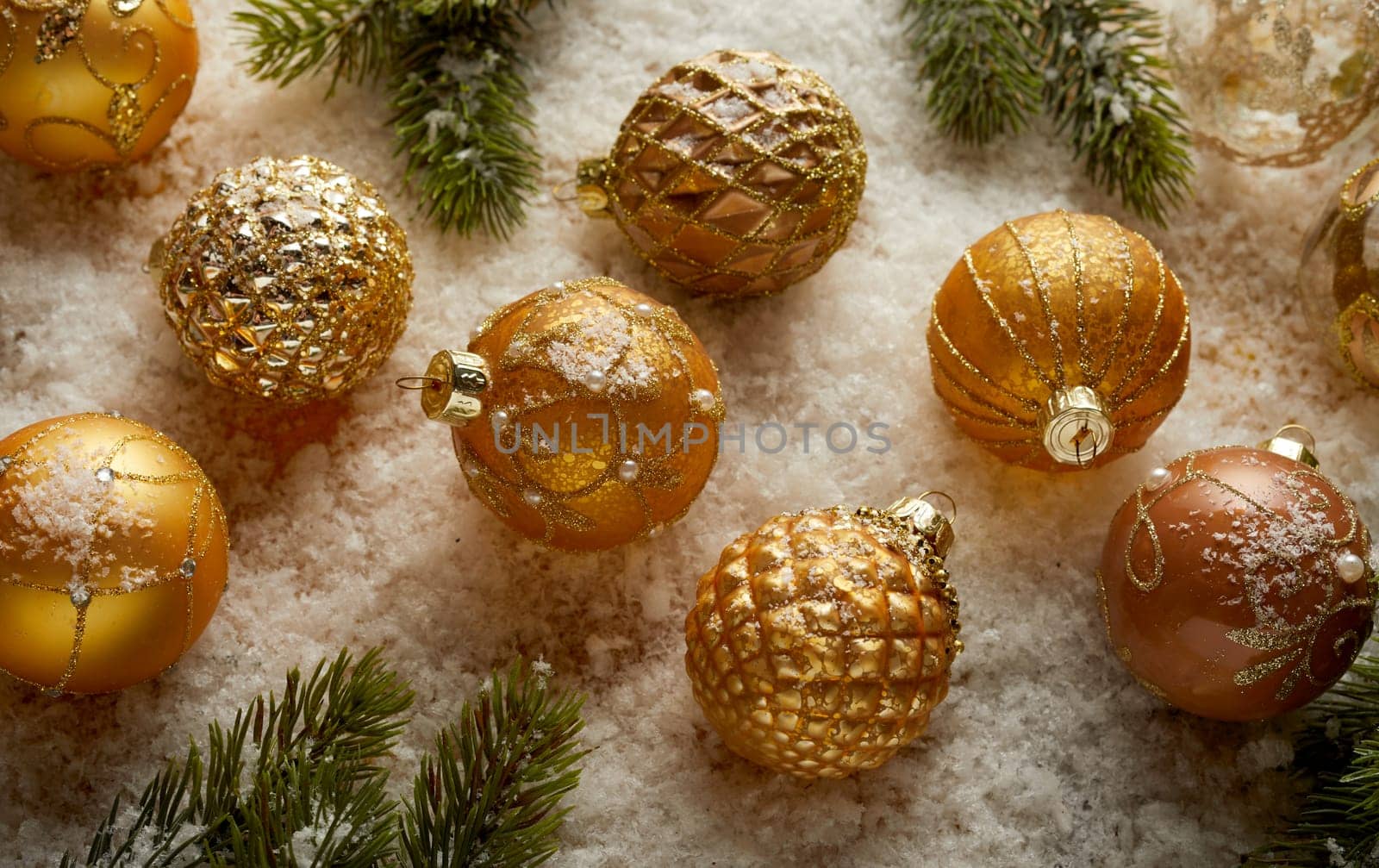 High angle of various golden Christmas baubles and green spruce branches arranged on white soft background
