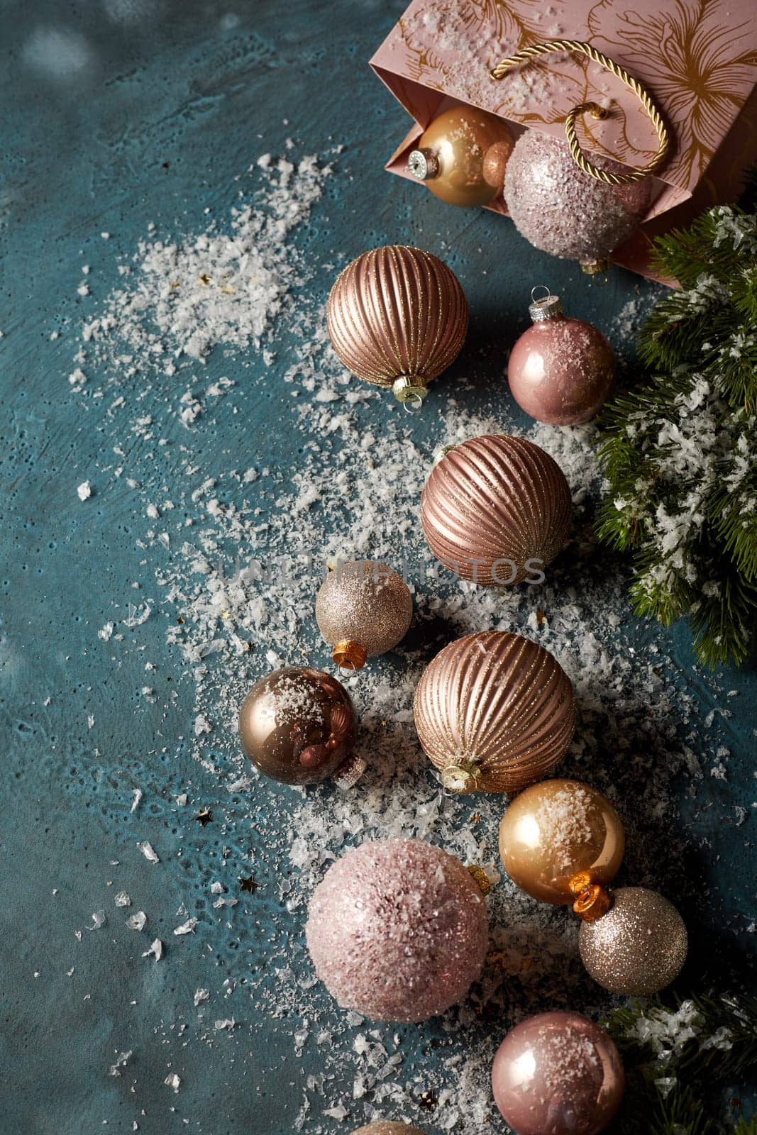 Top view of various shimmering Christmas balls and gift bag placed on artificial snow on black background