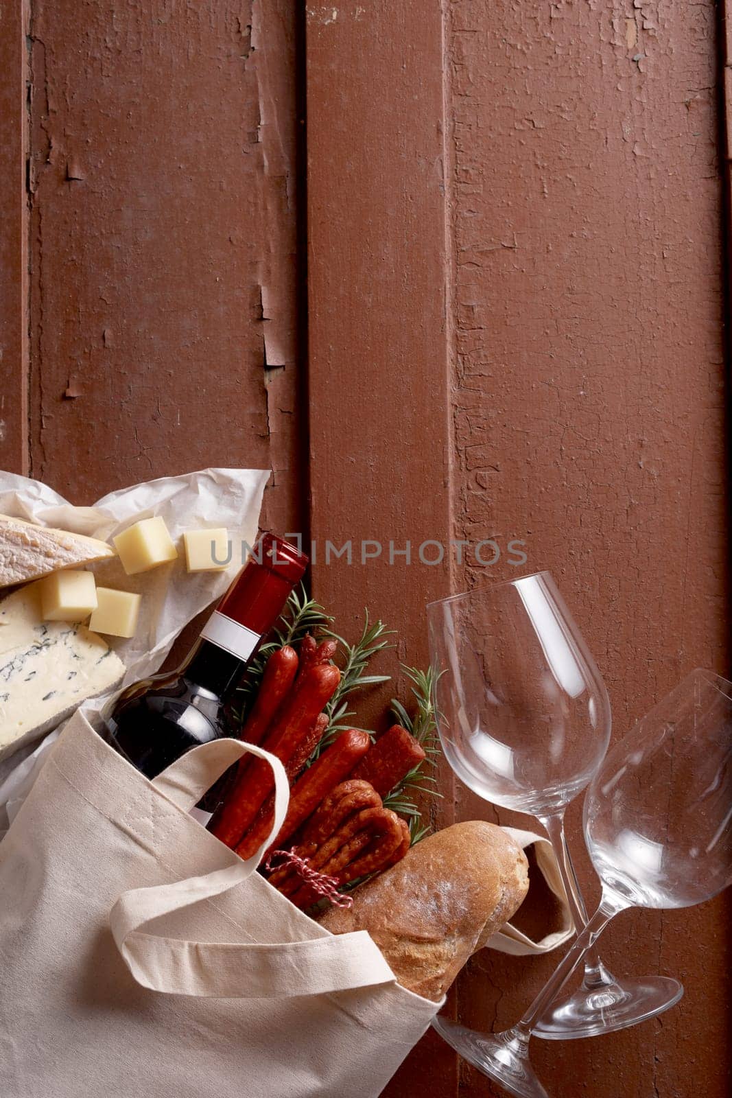 Top view of baguette and bottle of red wine placed on wooden table with wineglasses and cheese