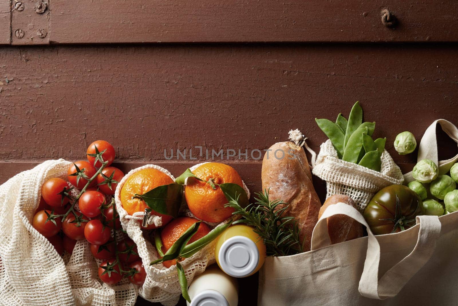 From above of fresh various groceries in eco friendly textile bags arranged on wooden table