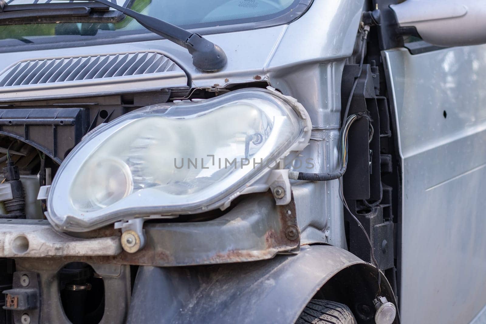 Broken headlights as a result of a collision. Broken gray car after an accident. Car accident concept. Damaged emergency headlight, hood and bumper. Damage to the car body after the accident
