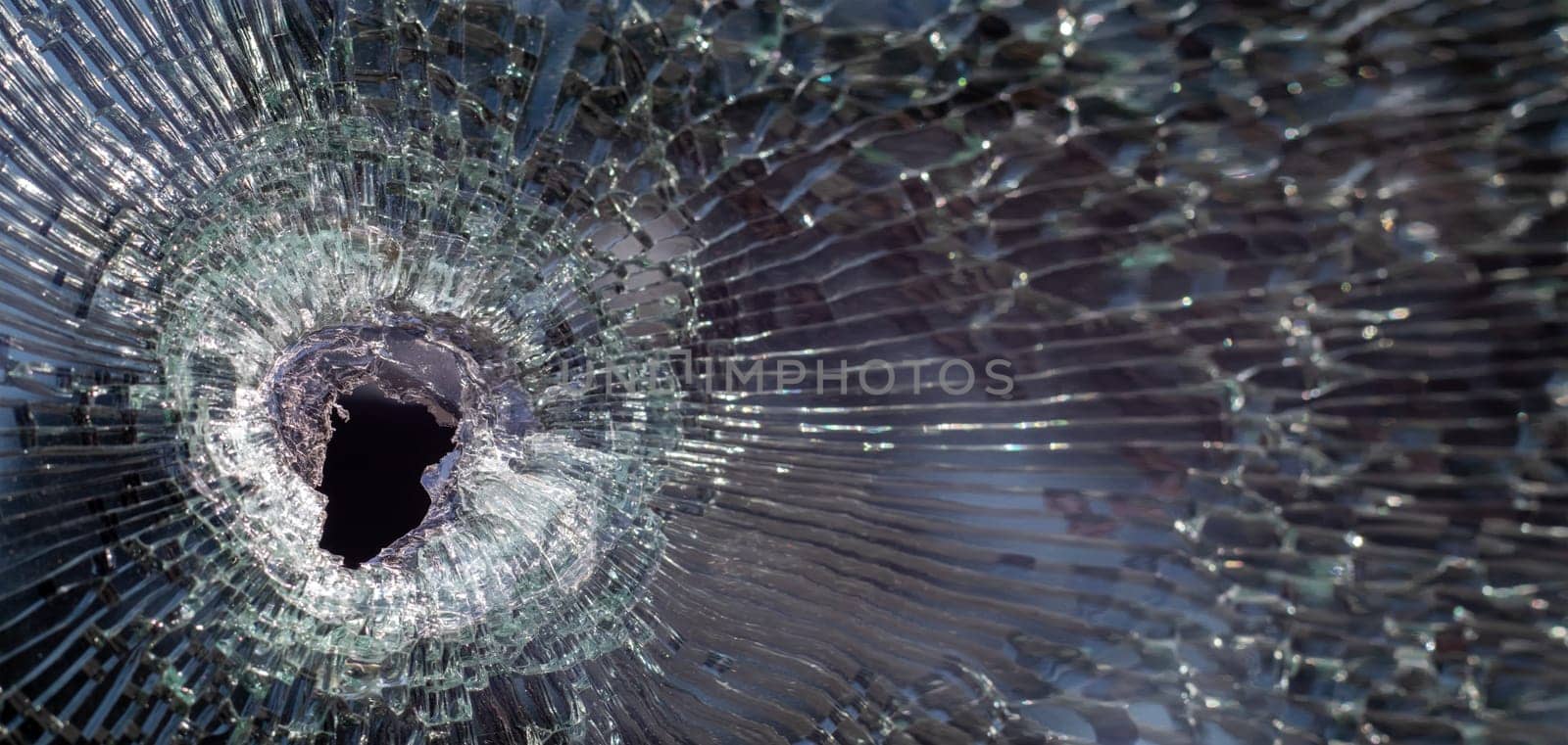 Bullet hole in glass with cracks, real bullet hole close-up. The bullet made a cracked hole in the windshield of a car or a window glass shattered as a result of an accident. Banner with copy space