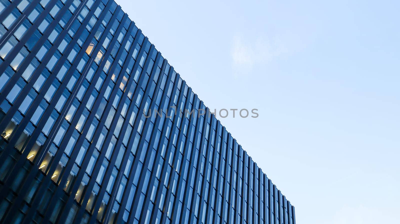 Modern high-rise building against the blue sky. Bottom view of a skyscraper in the business district. Low angle view of the glass facade of an office building