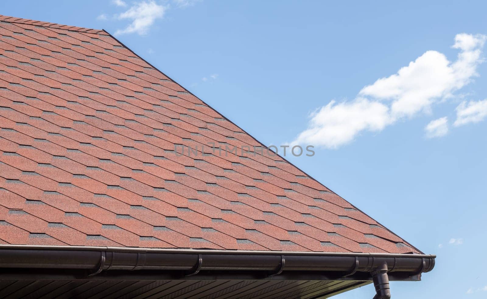 New roof with red shingles against the blue sky. High quality photo. Tiles on the roof of the house. Use to advertise roof fabrication and maintenance. Spotted texture. Affordable roofing