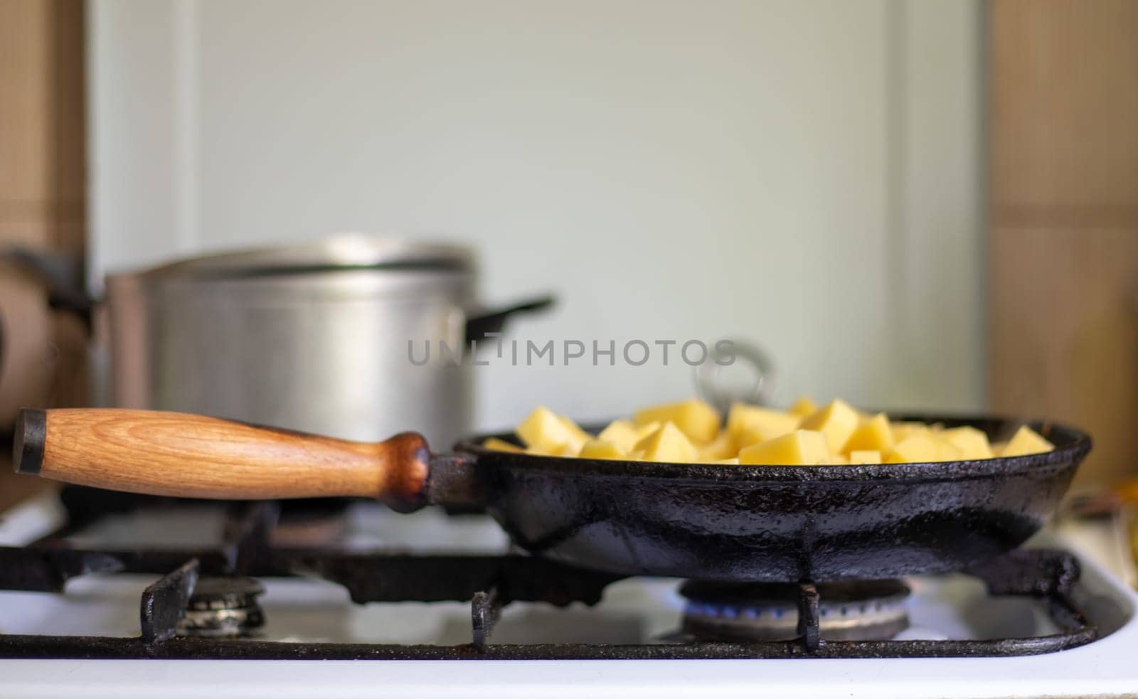 Roasting fresh potatoes in a cast iron skillet with sunflower oil. A view of a stovetop with a frying pan filled with golden fried potatoes in a real kitchen. Food cooked in a homemade frying pan
