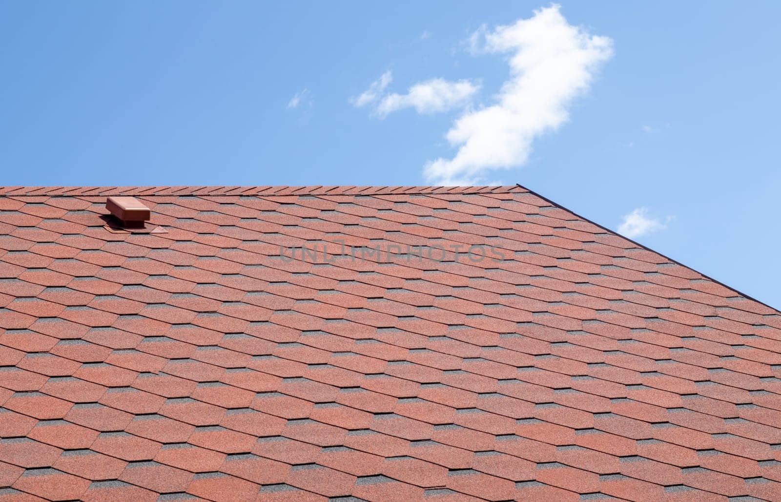 New roof with red shingles against the blue sky. High quality photo. Tiles on the roof of the house. Use to advertise roof fabrication and maintenance. Spotted texture. Affordable roofing