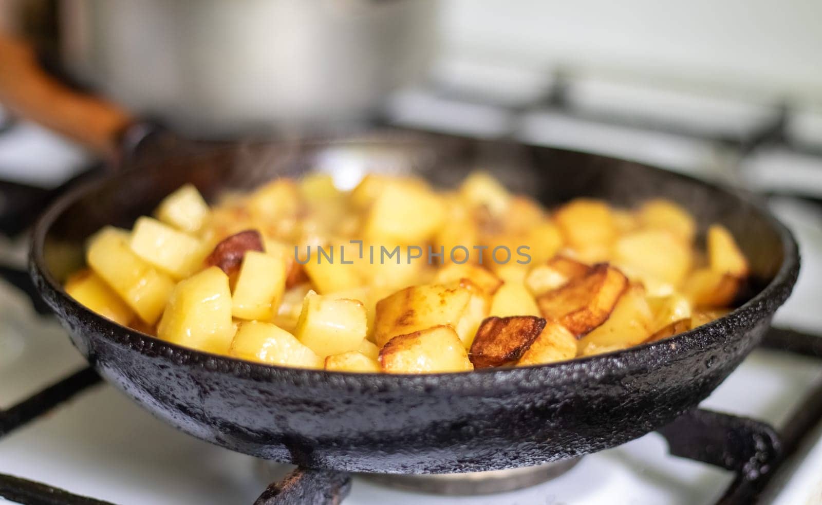 Roasting fresh potatoes in a cast iron skillet with sunflower oil. A view of a stovetop with a frying pan filled with golden fried potatoes in a real kitchen. Food cooked in a homemade frying pan