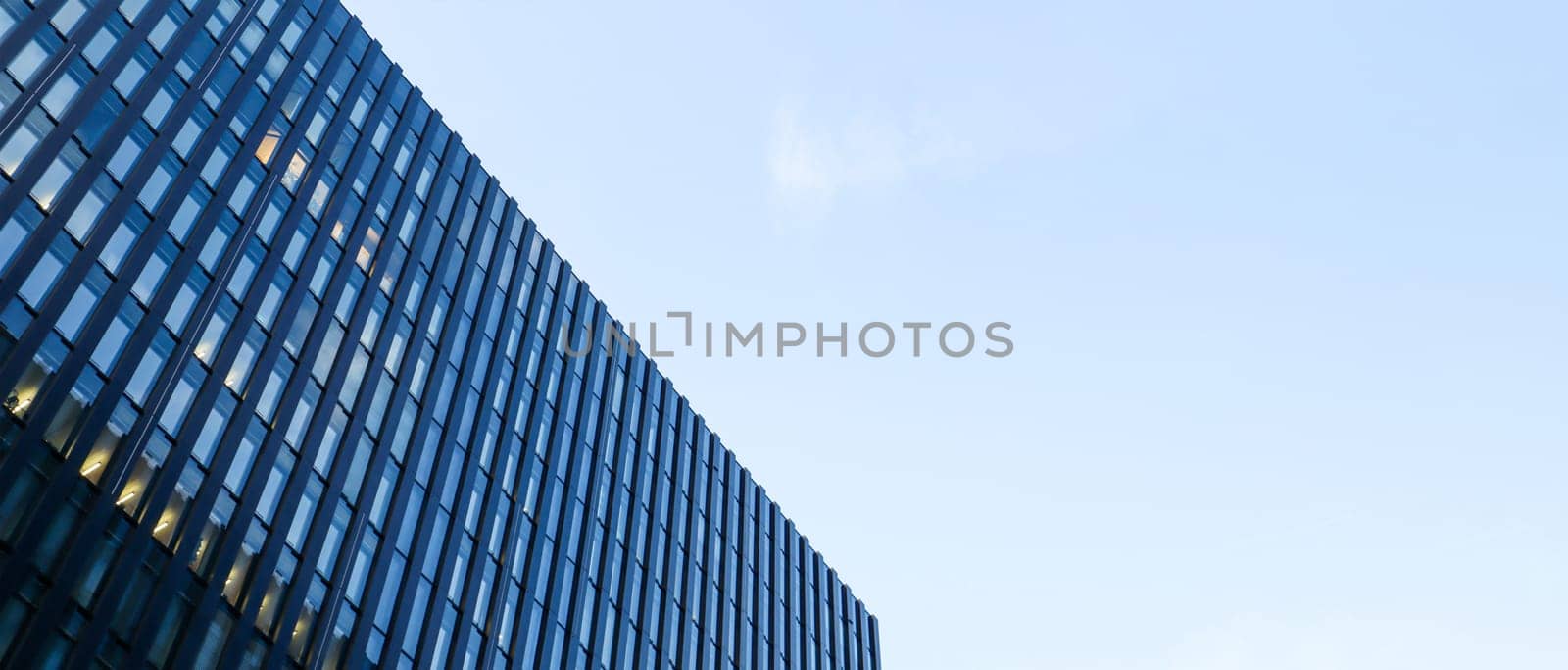 Modern high-rise building against the blue sky. Bottom view of a skyscraper in the business district. Low angle view of the glass facade of an office building. Banner with copy space