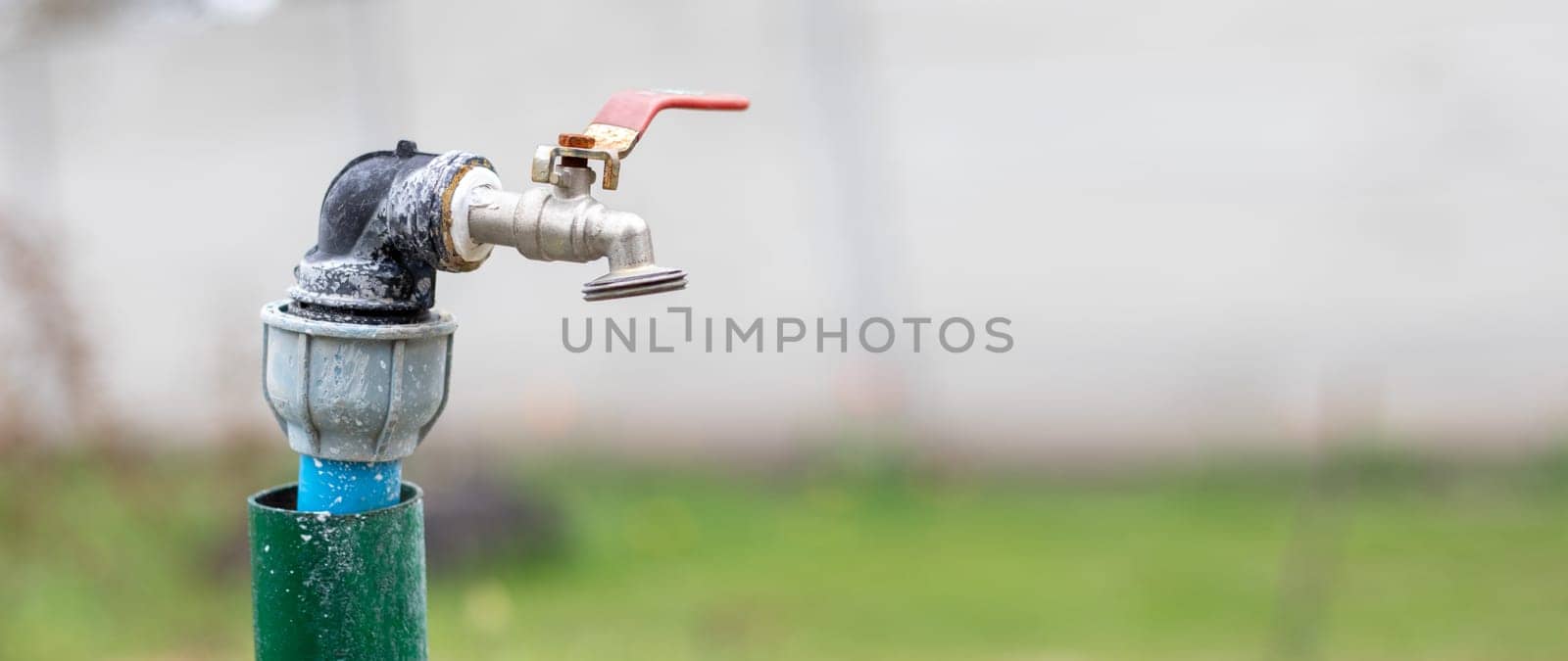 Water faucet on the background of nature. Opening or closing a faucet to save water indicates a water shortage problem. Selective focus with blurred background. Banner with copy space