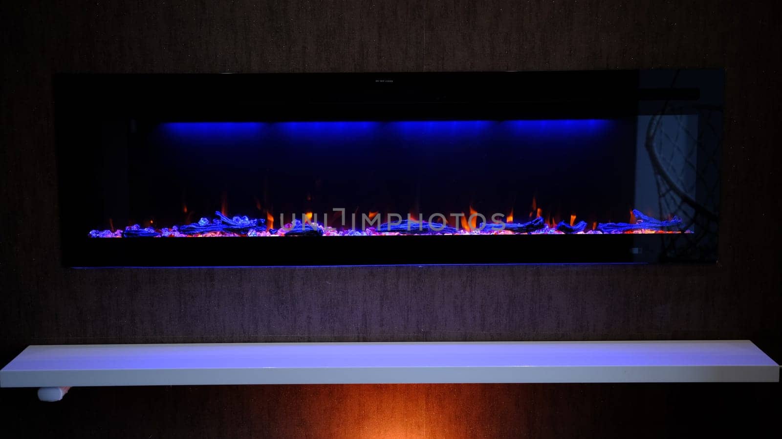 view on electric fireplace with artificial sparkling flame, decor for the interior, orange flame on crystals with blue and orange backlighting
