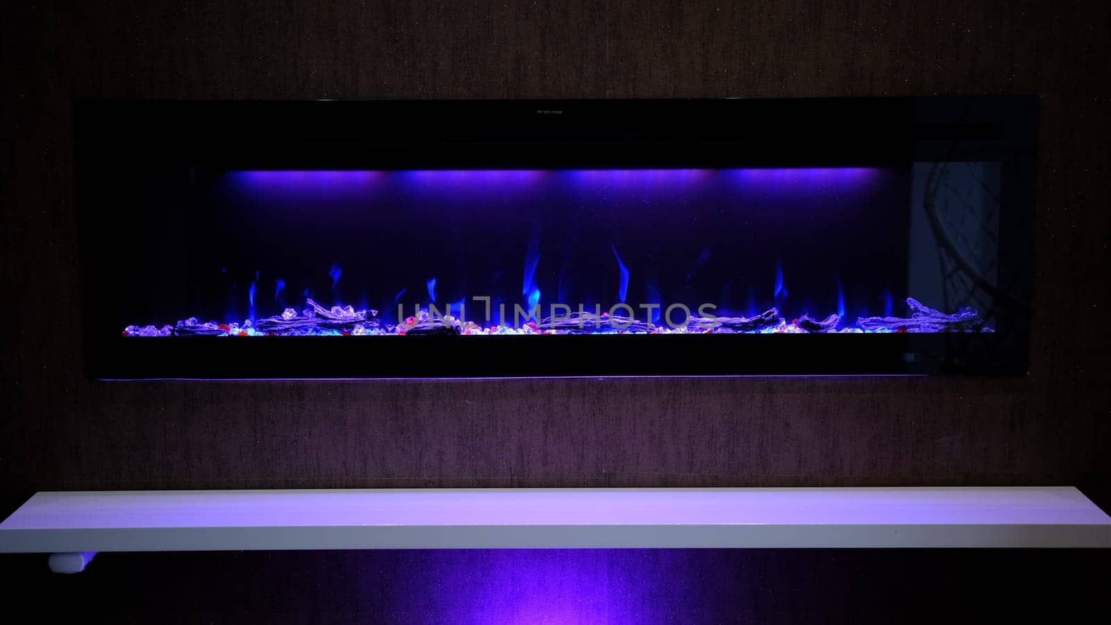 view on electric fireplace with artificial sparkling flame, decor for the interior, blue flame on crystals with violet purple backlighting.