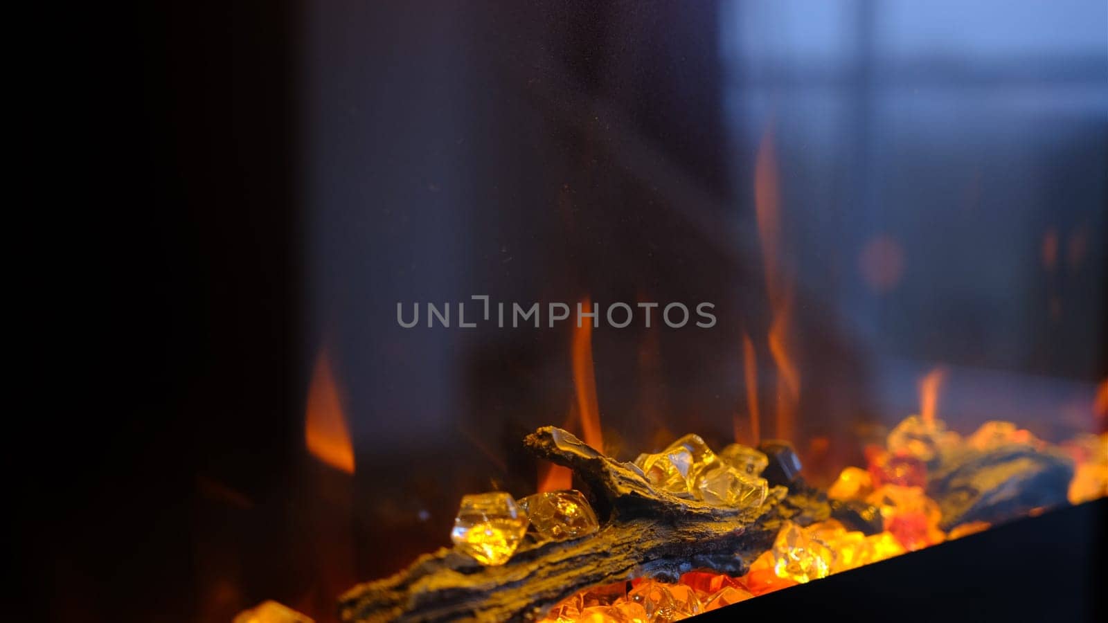 Side view on electric fireplace with artificial sparkling flame, decor for the interior, blue and orange flame with suspended swing chair in reflection.