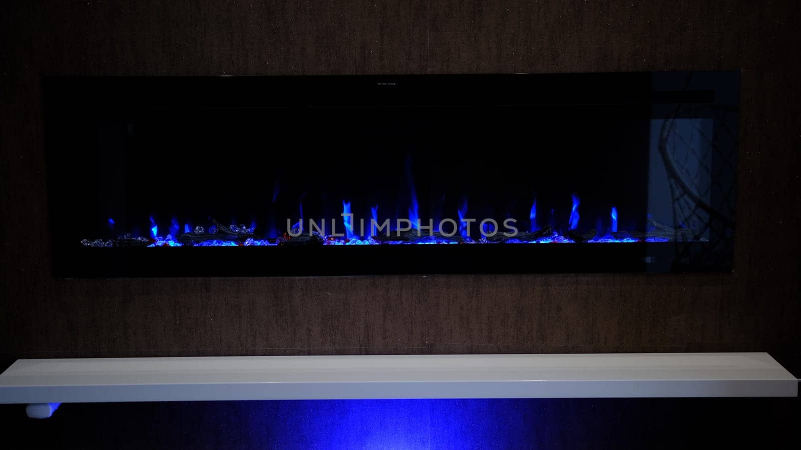 view on electric fireplace with artificial sparkling flame, decor for the interior, blue flame on crystals with blue backlighting.