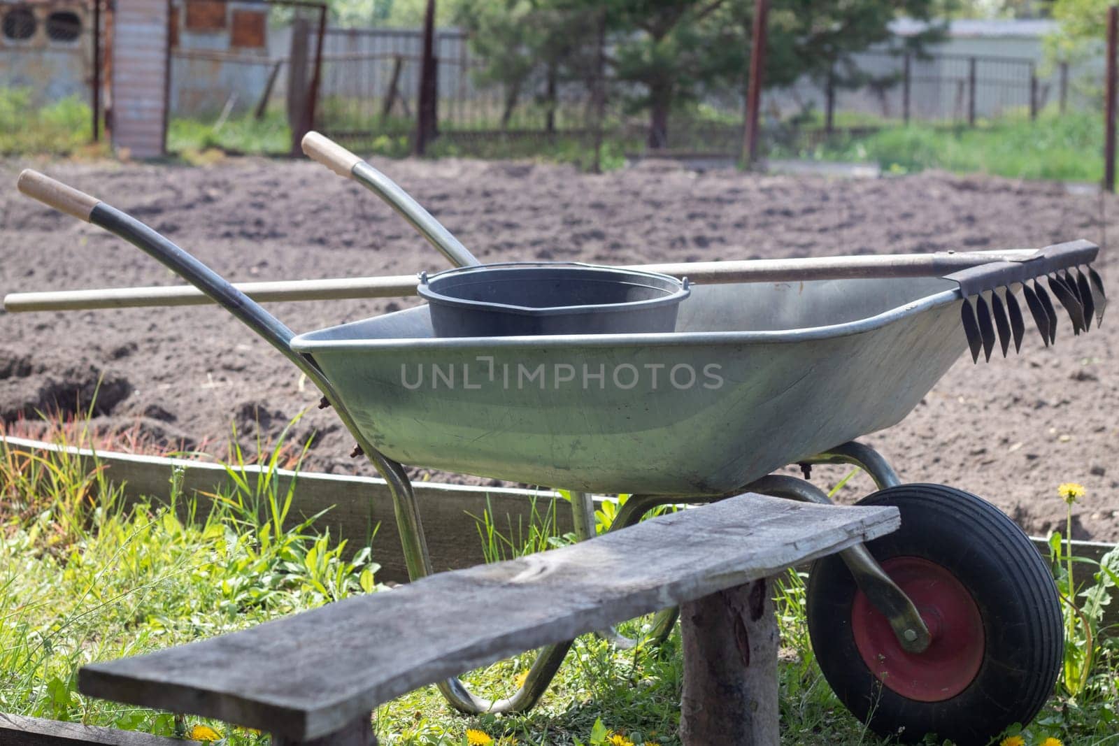 Gray metal garden wheelbarrow with two handles and one wheel. The wheelbarrow is in the garden or garden. Gardener's wheelbarrow in the backyard. Garden cleaning